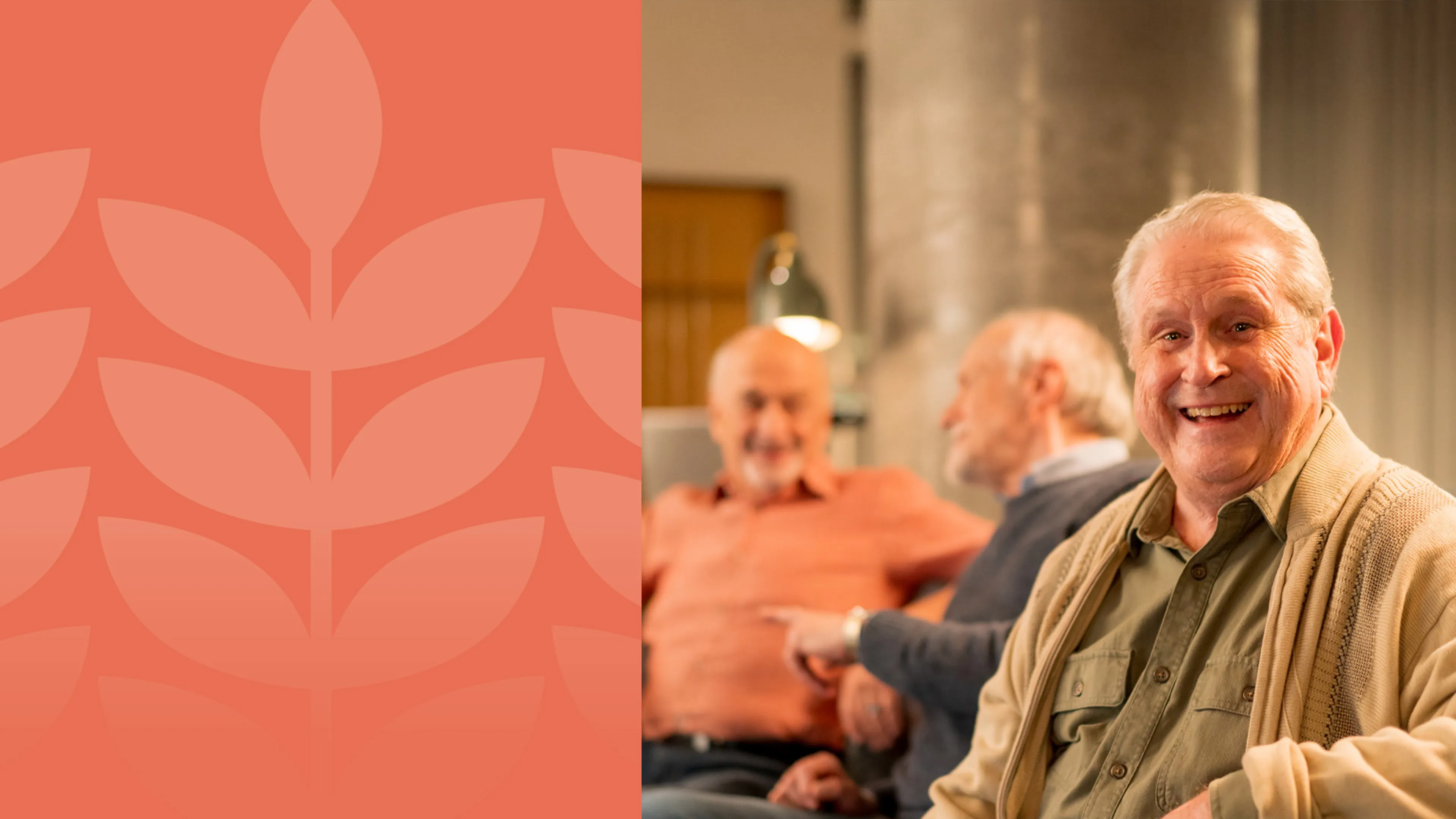 A group of senior gentlemen sit on a couch in a lounge, smiling and chatting with each other.