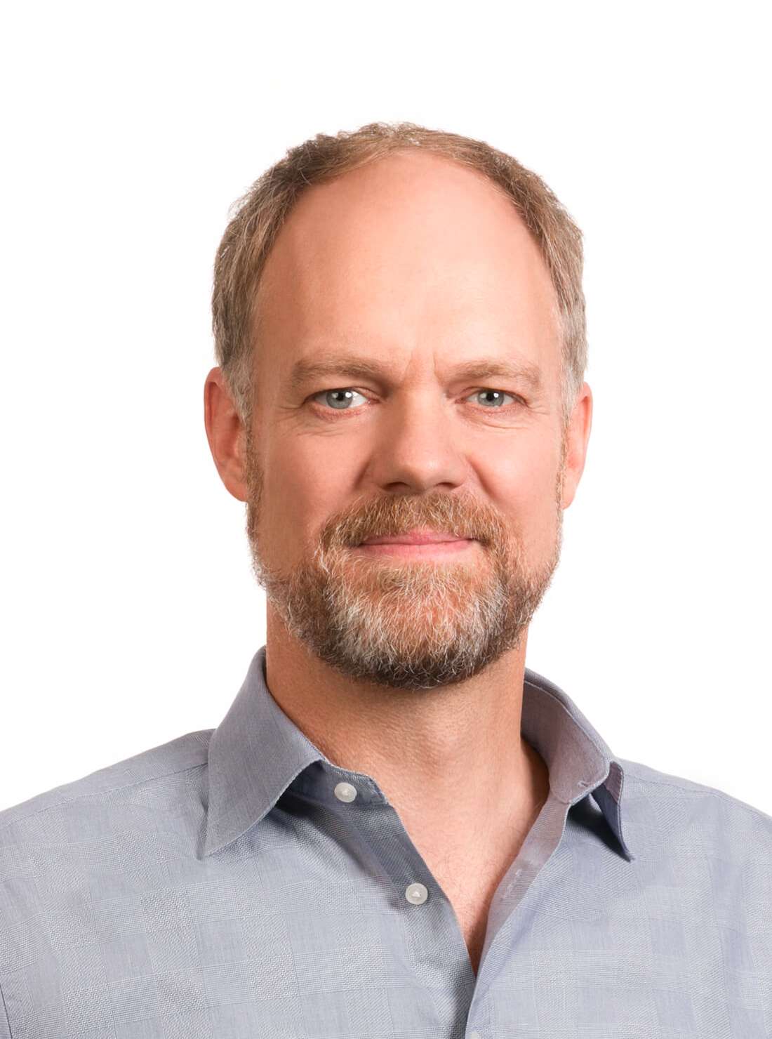 Headshot of a smiling man, Peter Mitchell, with a light beard, wearing a light blue collared shirt.