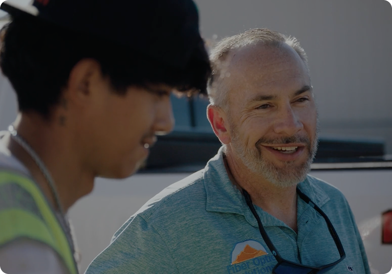 Two male workers smiling outdoors.