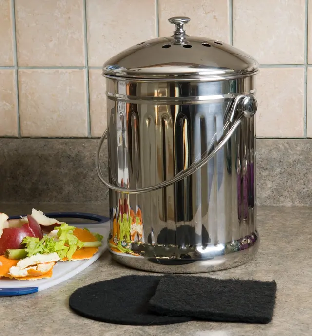 Seau à compost sur un comptoir près de restes de légumes et de filtres