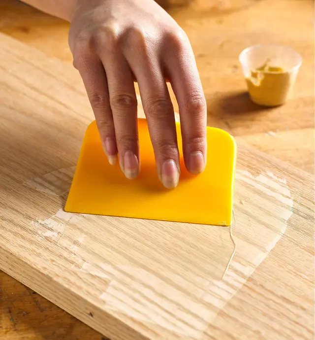 Spreading wood filler on a board to fill the grain
