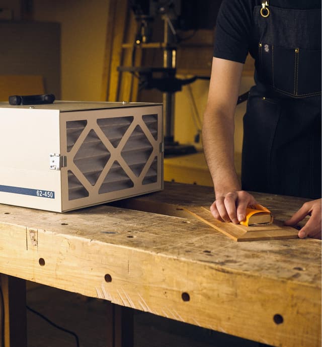 Rikon 450 cfm air cleaner on a workbench next to a board that a man is sanding