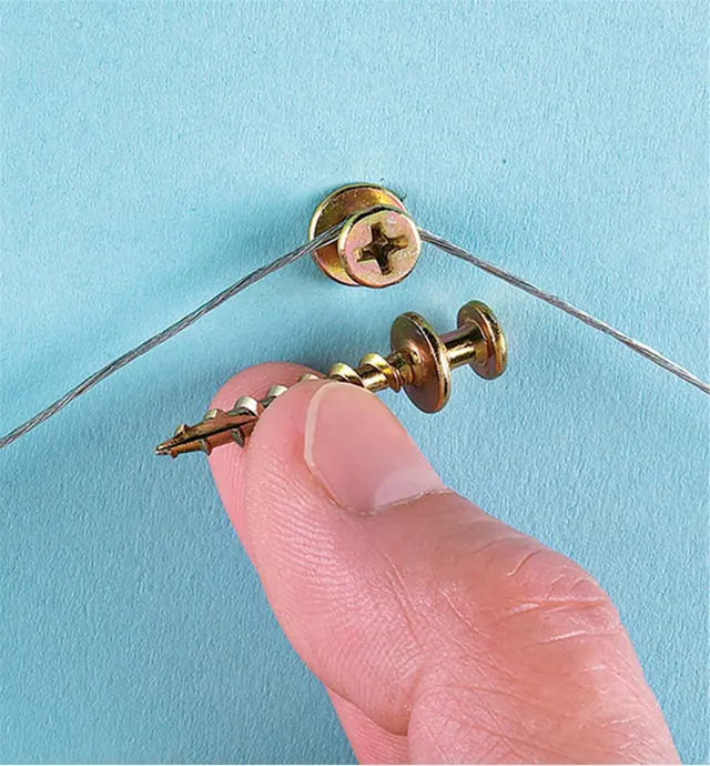 Bear Claw Screw installed in a wall, holding a picture wire, next to another screw being held between two fingers to show its profile