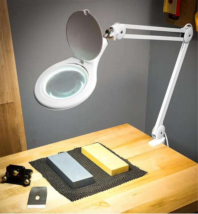 Lamp clamped to a workbench, illuminating two water stones, a plane blade and a sharpening jig