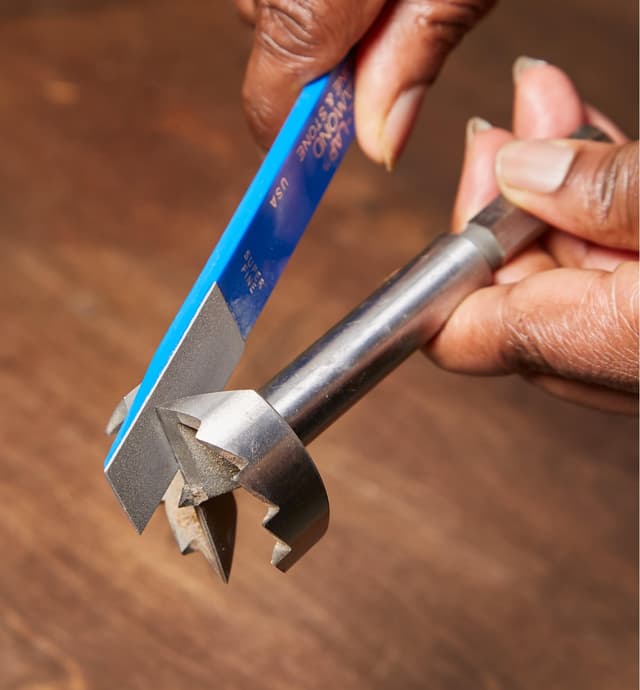 Personne utilisant un petit affiloir diamanté pour affûter une mèche à arêtes dentées)