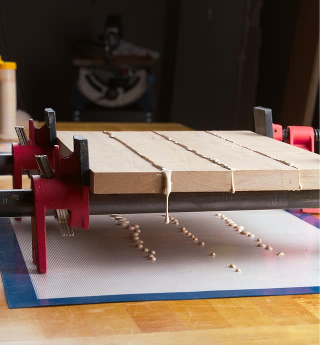 Pièces de bois fraîchement collées séchant dans des serre-joints par-dessus un tapis protecteur en silicone