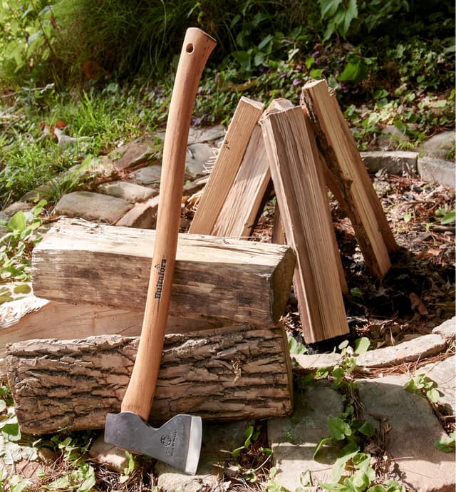 Small forest axe leaning against a stack of logs next to a fire pit