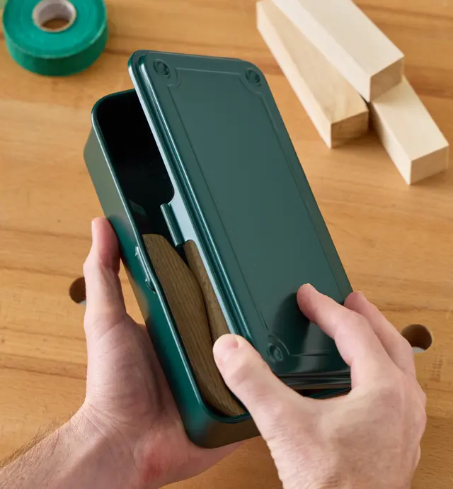 Personne qui ouvre une boîte de rangement verte contenant de petits outils manuels
