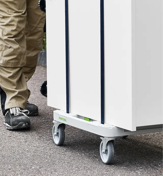 Une personne pousse une armoire attachée avec des sangles sur un chariot Sys-Cart.