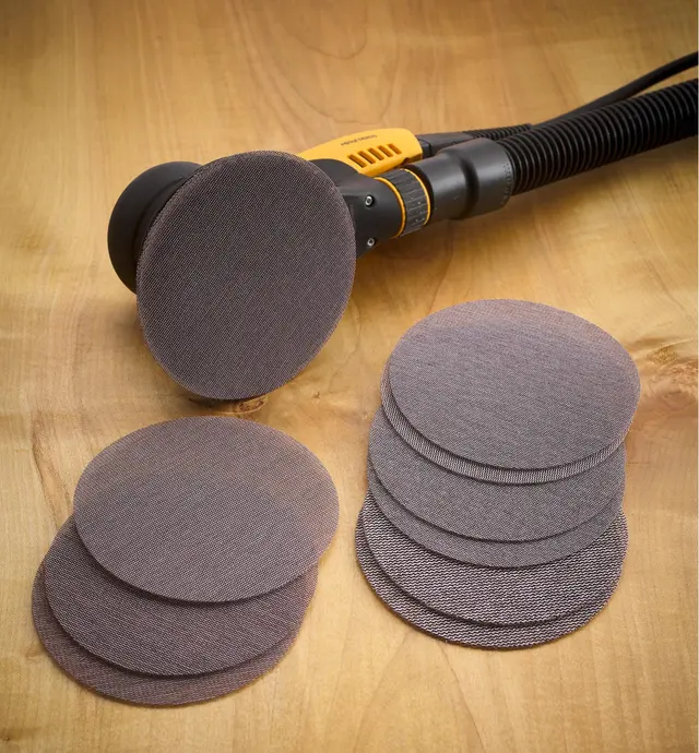 Plusieurs disques abrasifs autoagrippants Abranet devant une ponceuse orbitale Mirka