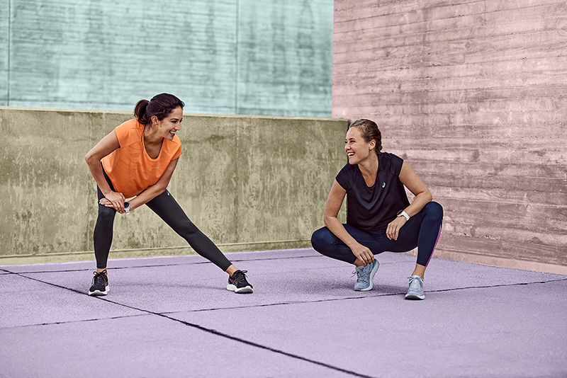 Two runners in ASICS shoes and clothing performing a knee stretch
