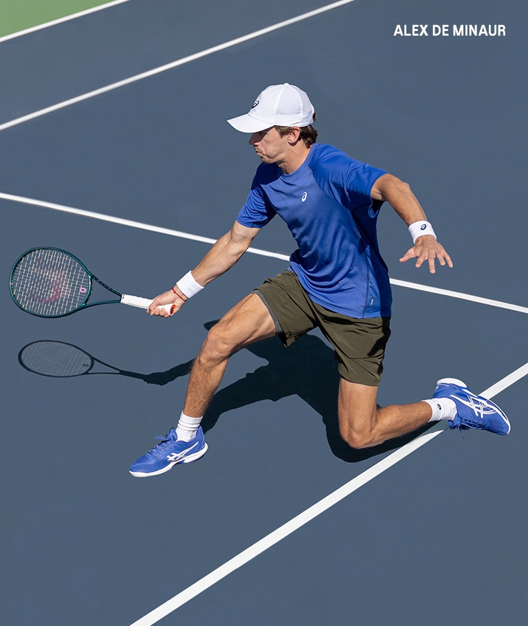Alex de Minaur playing tennis wearing blue ASICS shoes.