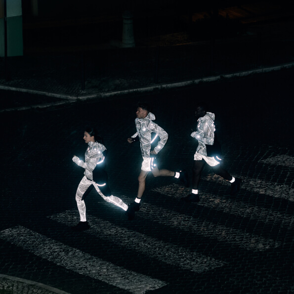 Three runners on a pedestrian crosswalk wearing limited series reflective running tops tights and shorts.