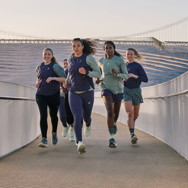Women wearing ASICS Nagino clothing and running on a bridge.