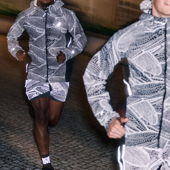 Two men running at night in the city wearing reflective running jackets and shorts.