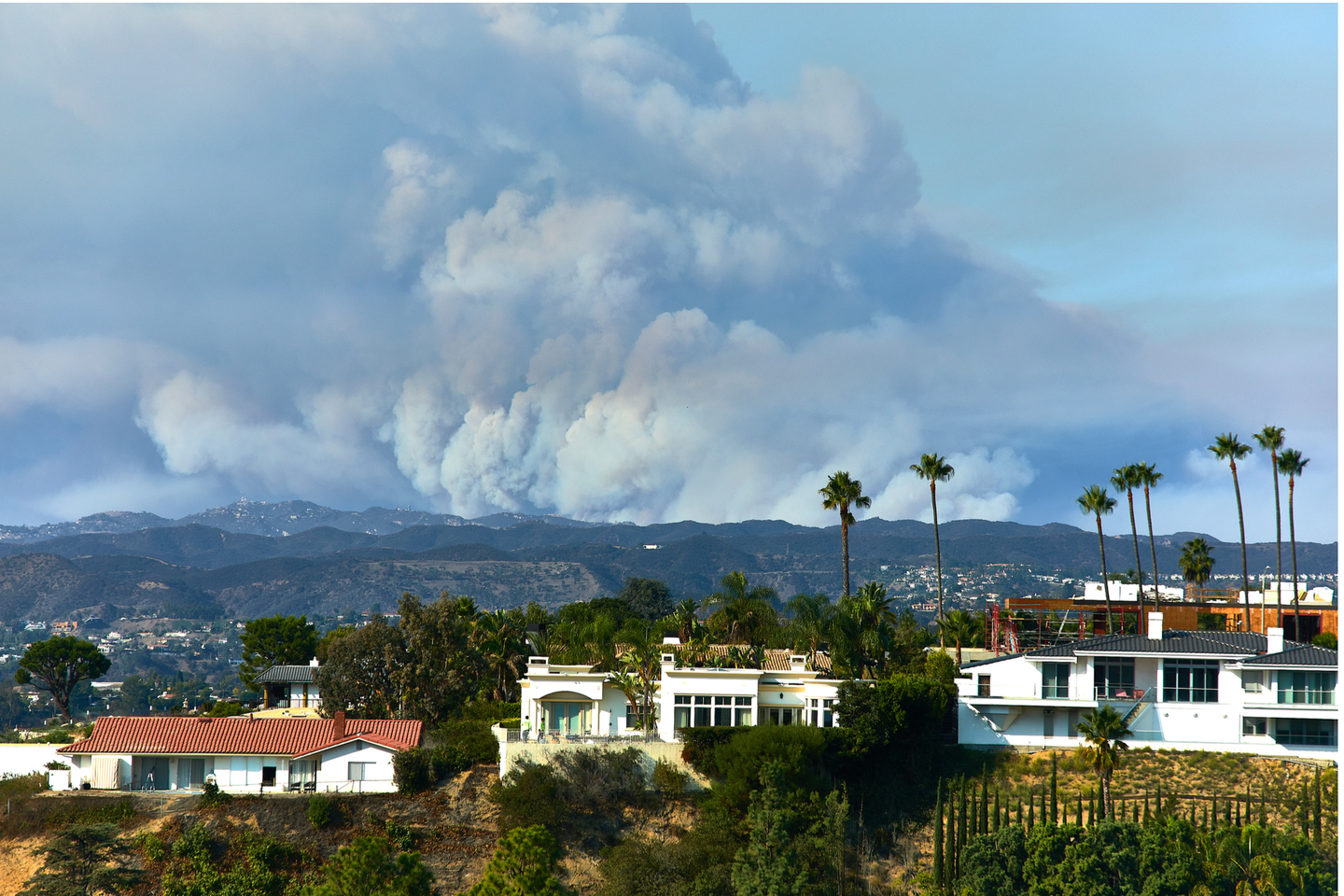 Photo of houses with fire smoke in the background of hills