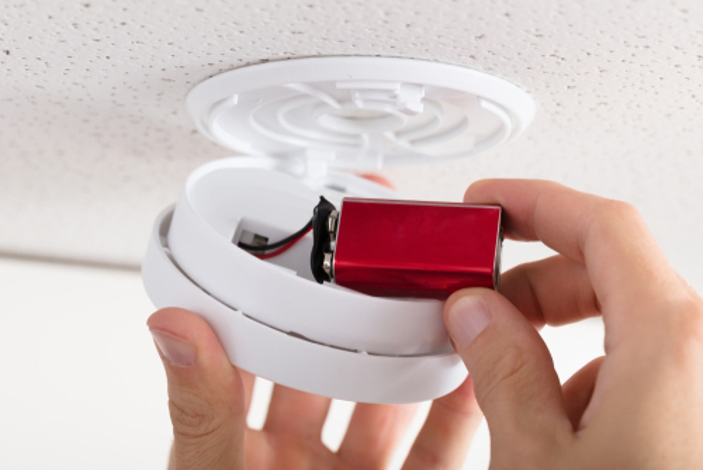 Close up of hand changing a red battery in a white smoke detector