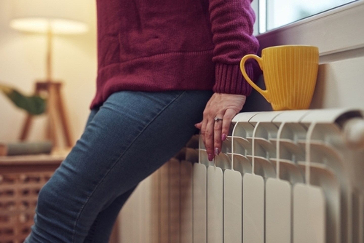 Woman in red sweater and jeans leaning on a heat radiator