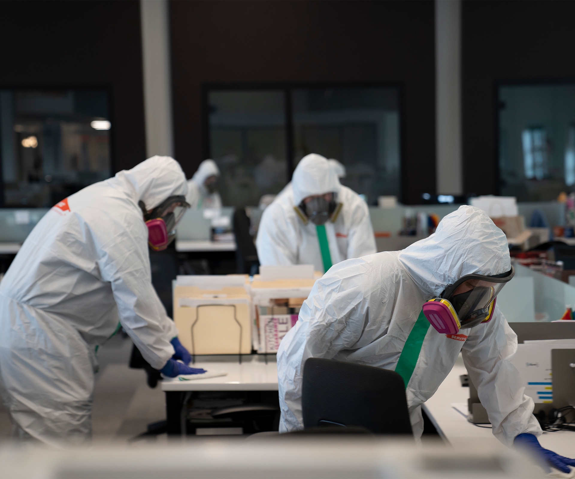 Workers in hazmat suits cleaning desks in commercial office space
