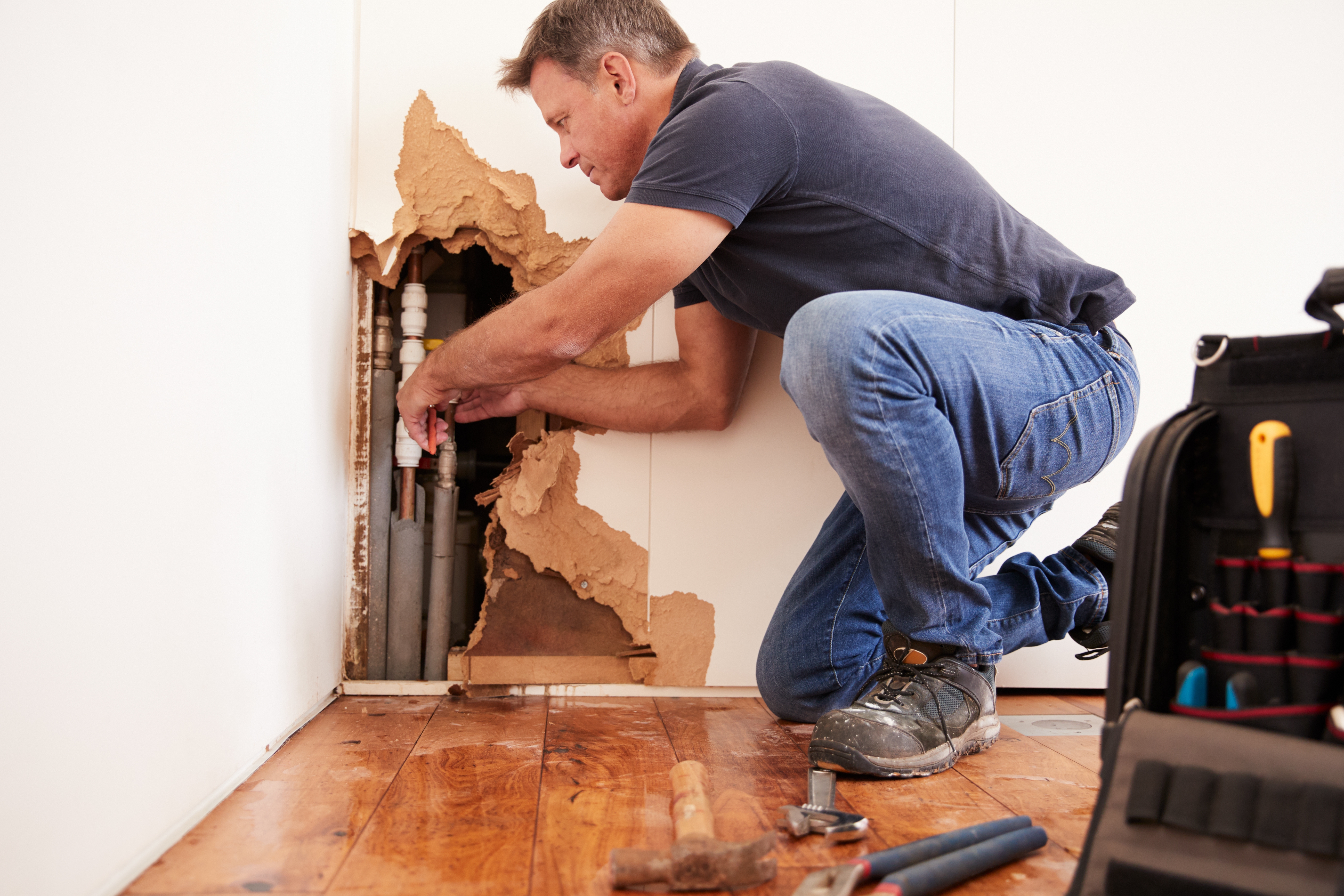 A plumber fixes broken pipes inside a wall