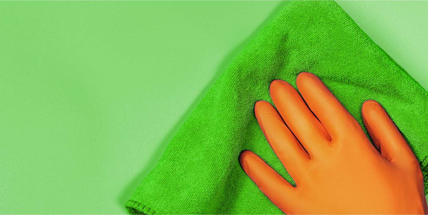 Orange glove being used to wipe green background with green cloth