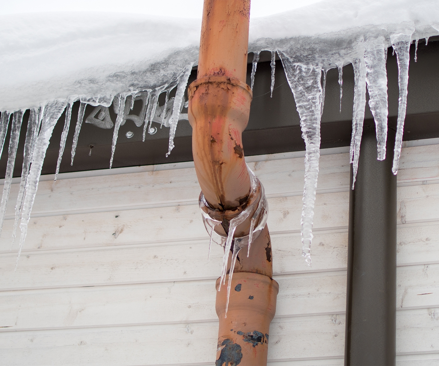 Roof having icicles coming off of it with a drain pipe leaking but frozen