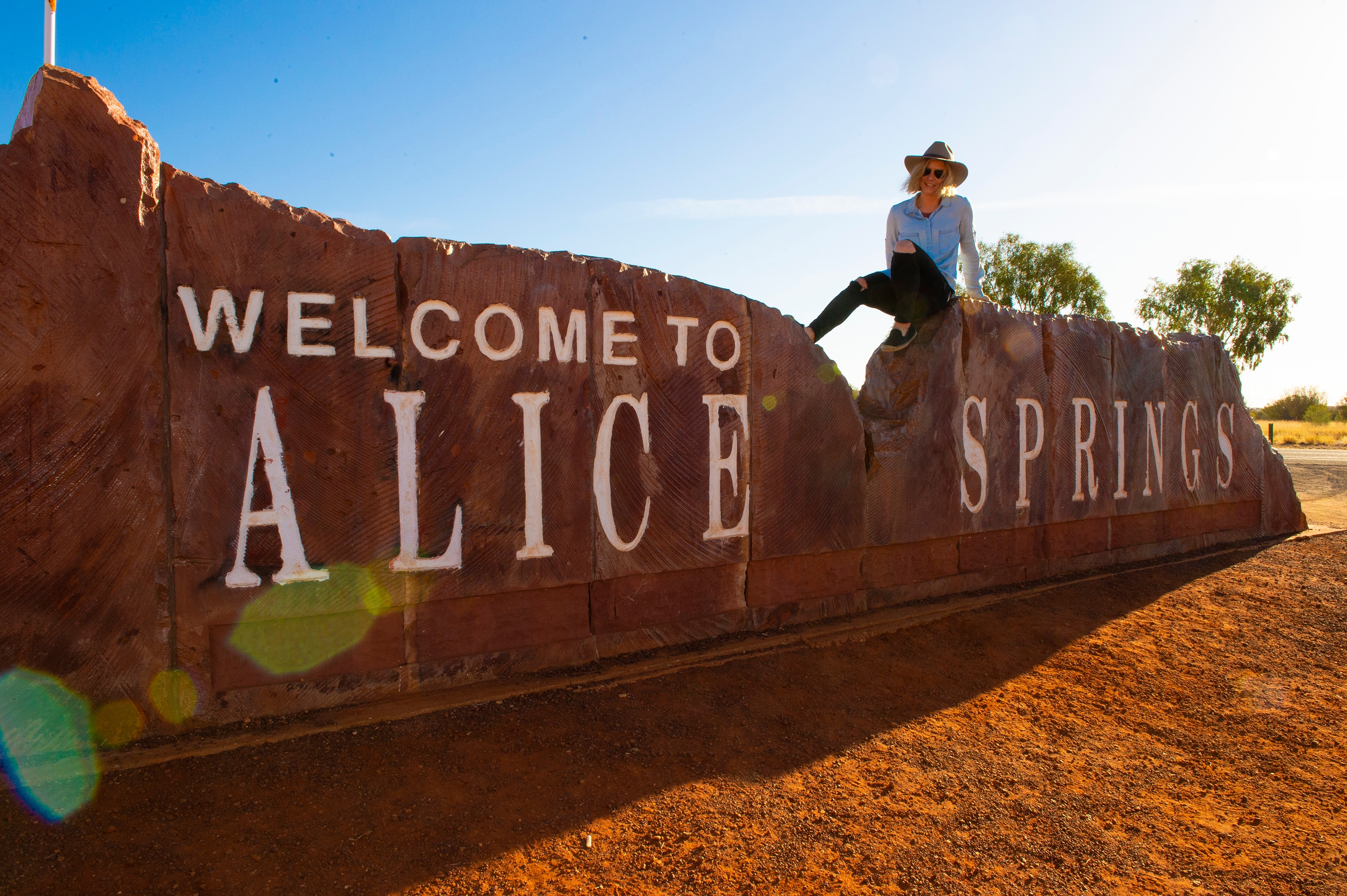 Woman sitting on the Welcome to Alice Springs sign