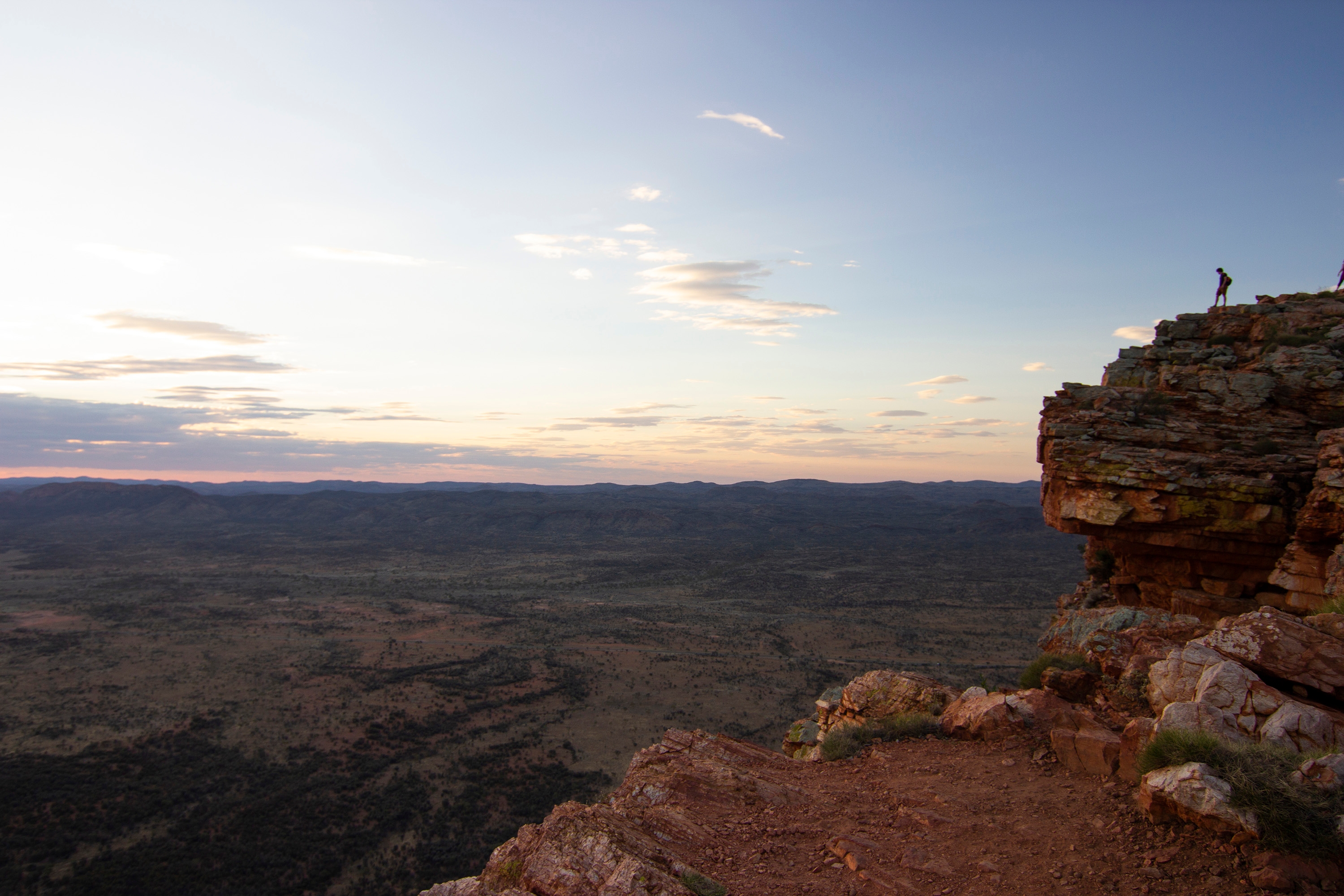 Man up on a rock escarpment looking over West MacDonnell Ranges