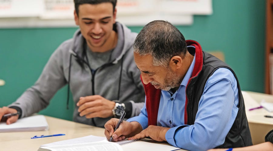Un adulto aprendiendo inglés junto a un joven que lo ayuda.