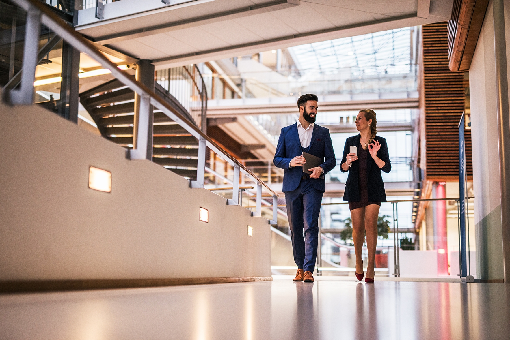 Un hombre y una mujer hablando de negocios caminando en una oficina.