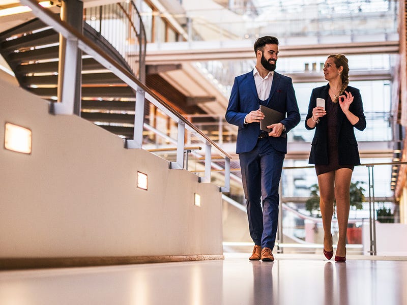 Un hombre y una mujer hablando de negocios caminando en una oficina.