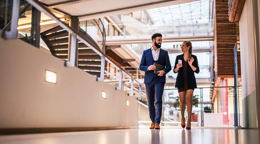 Un hombre y una mujer hablando de negocios caminando en una oficina.
