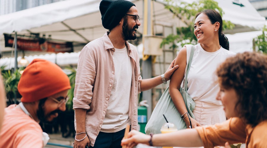 Joven saludando a su grupo de amigos tomando un café en la calle.