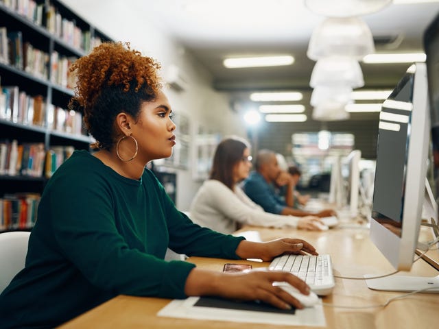 African American lady is studying at a library computer immersing herself in language study and understanding how to learn a language fast.