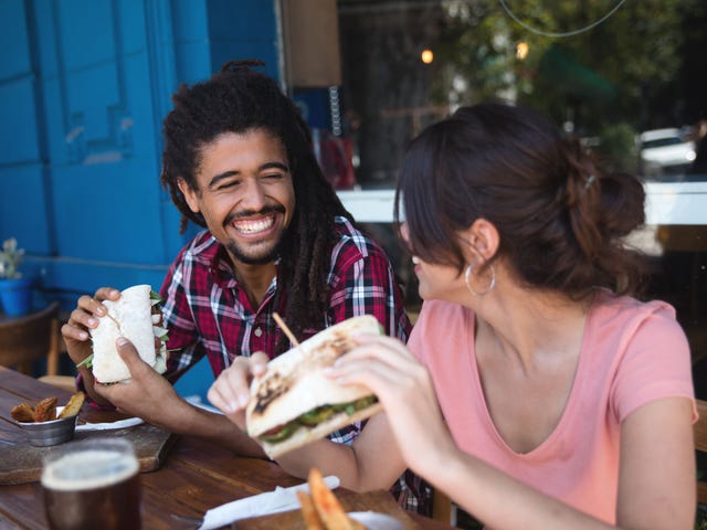 A happy young man with dreadlocks having a sandwich lunch with a smiling new female friend in a pink t-shirt, a shining example of how to make friends in a new country.