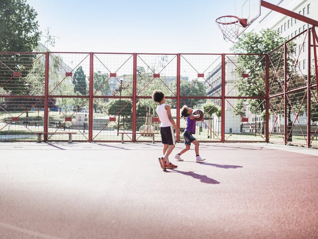 Two young boys playing basketball and enjoying the fun, active benefits of summer camp.