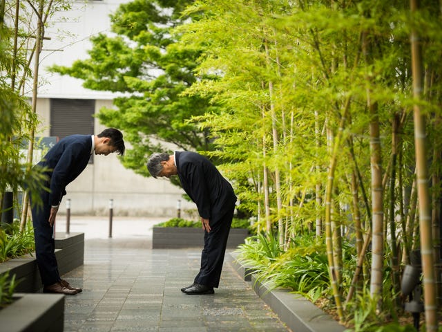 Colleagues greeting each other with a respectful bow, surrounded by bamboo trees - an example of cultural differences in communication.