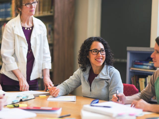 Happy multilingual female student with friend and teacher discussing the best careers for bilinguals, in a library.