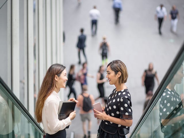 Two smiling well-dressed female employees on an escalator have overcome language barriers in the workplace.