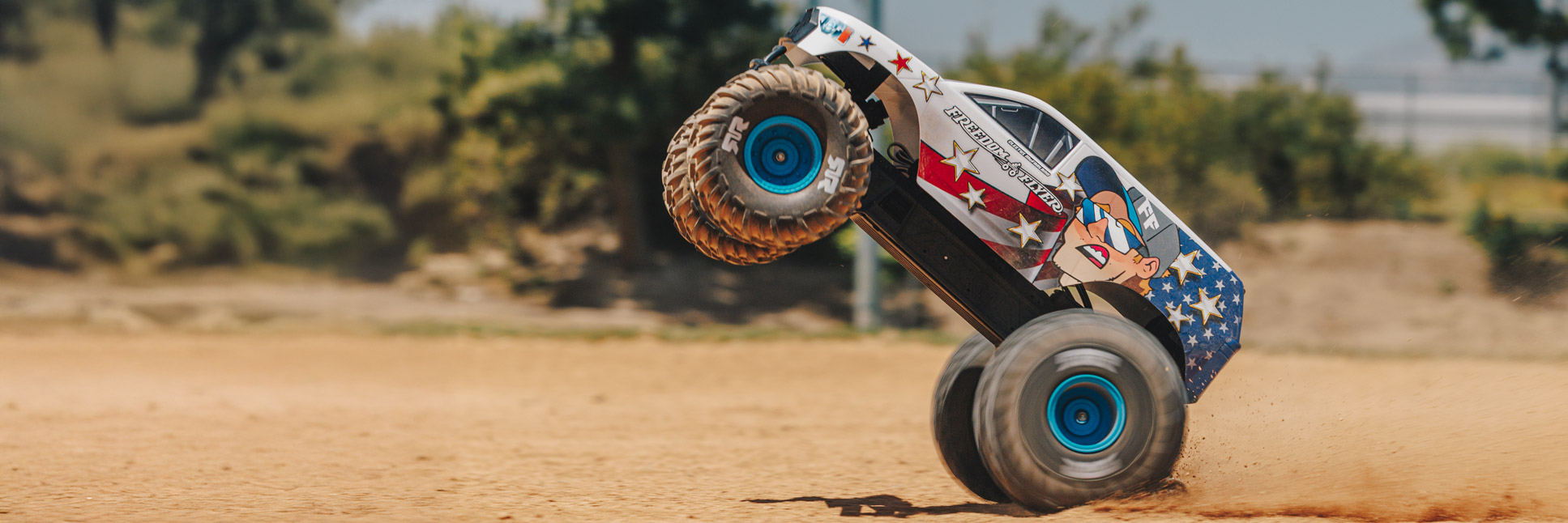 Action shot of the ARRMA Freedom Flyer RC Monster Truck bashing through the dirt with a plume of dust flying in the air