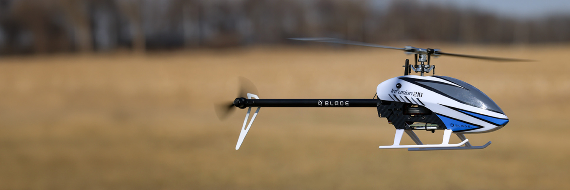Action shot of the Blade InFusion 210 Bind-N-Fly Basic RC helicopter with AS3X and SAFE hovering in the air above a field