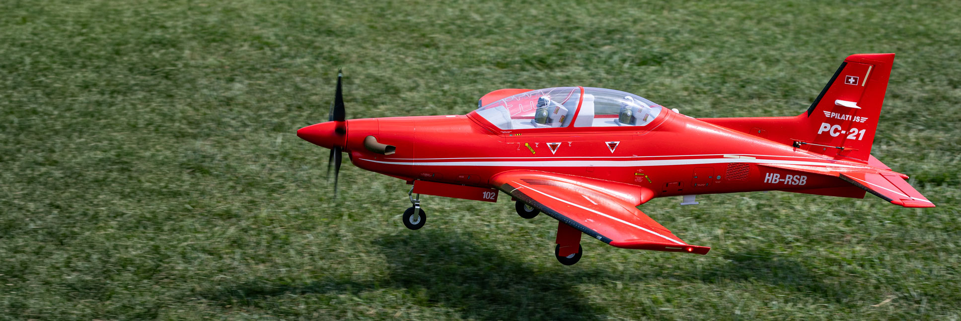 Action shot of the E-flite Pilatus PC-21 1.3m RC Aircraft flying in the air above a tarmac