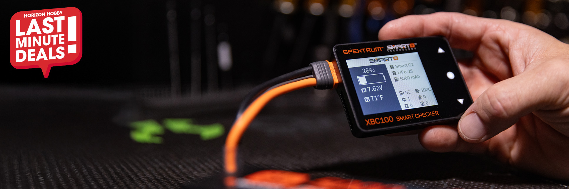 Action shot of a hand holding the XBC100 Smart LiPo Battery Checker & Servo Driver on their RC workbench with the Last Minute Deals logo