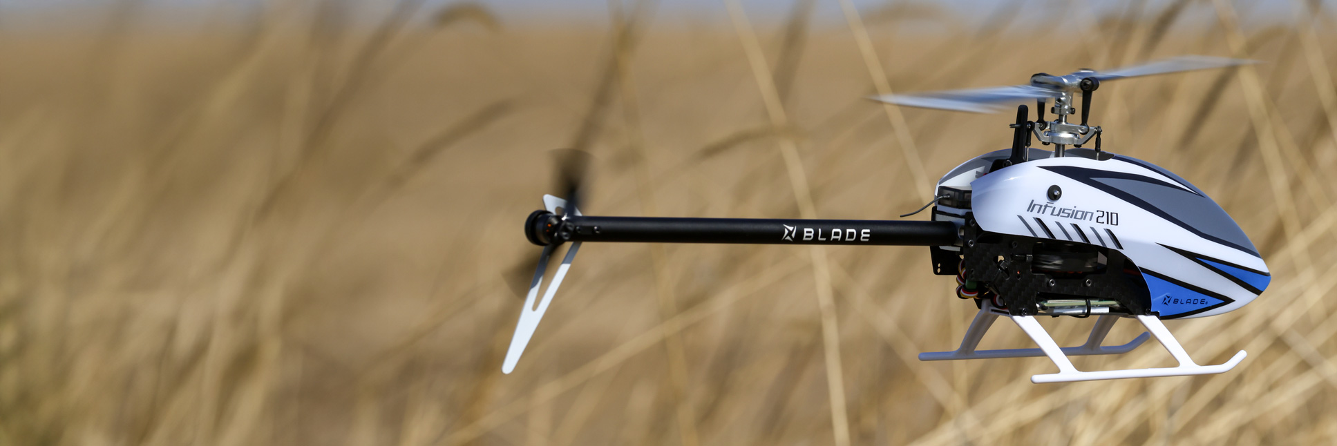 Action shot of the Blade InFusion 210 Bind-N-Fly Basic with AS3X and SAFE RC helicopter hovering in the air above a field Action shot of the Blade InFusion 210 Bind-N-Fly Basic with AS3X and SAFE RC helicopter hovering in the air above a field