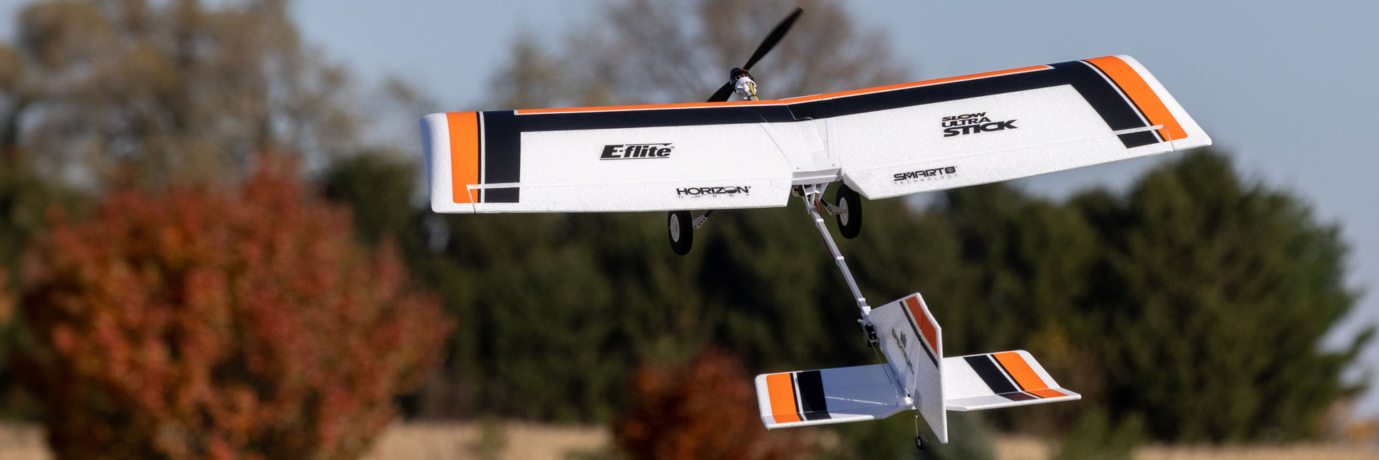 Action shot of the E-flite Slow Ultra Stick 1.2m BNF Basic with AS3X and SAFE Select RC Aircraft flying through the air above a grassy field Action shot of the E-flite Slow Ultra Stick 1.2m BNF Basic with AS3X and SAFE Select RC Aircraft flying through the air above a grassy field