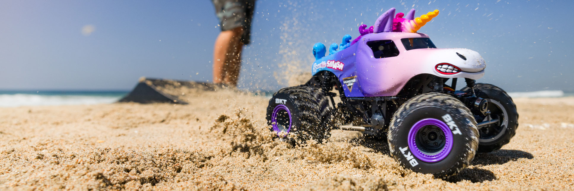 Action shot of the 1/18 Losi Mini LMT Sparkle Smash RC Monster Truck bashing through the sand on a beach