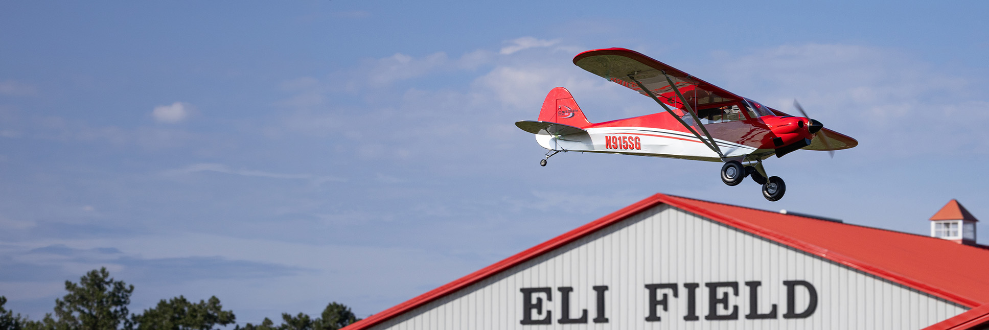 Action shot of the Hangar 9 Carbon Cub 15cc RC Airplane flying in the air above the Eli Field