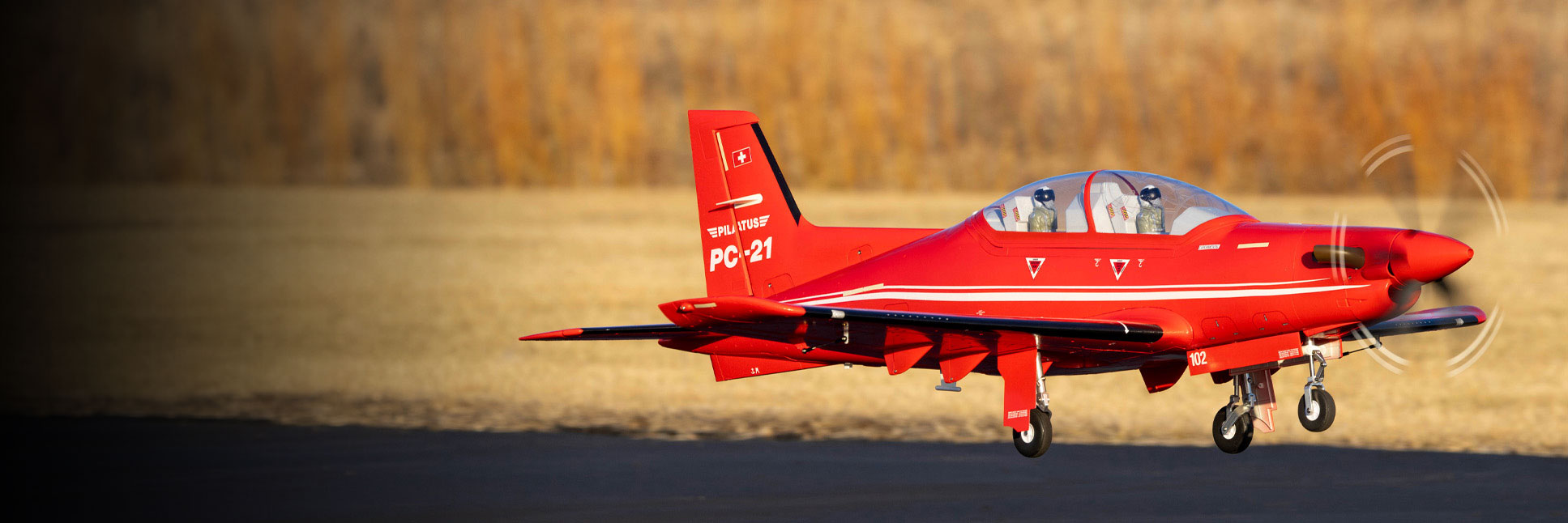 Action shot of the E-flite Pilatus PC-21 1.3m RC Aircraft flying in the air above a tarmac