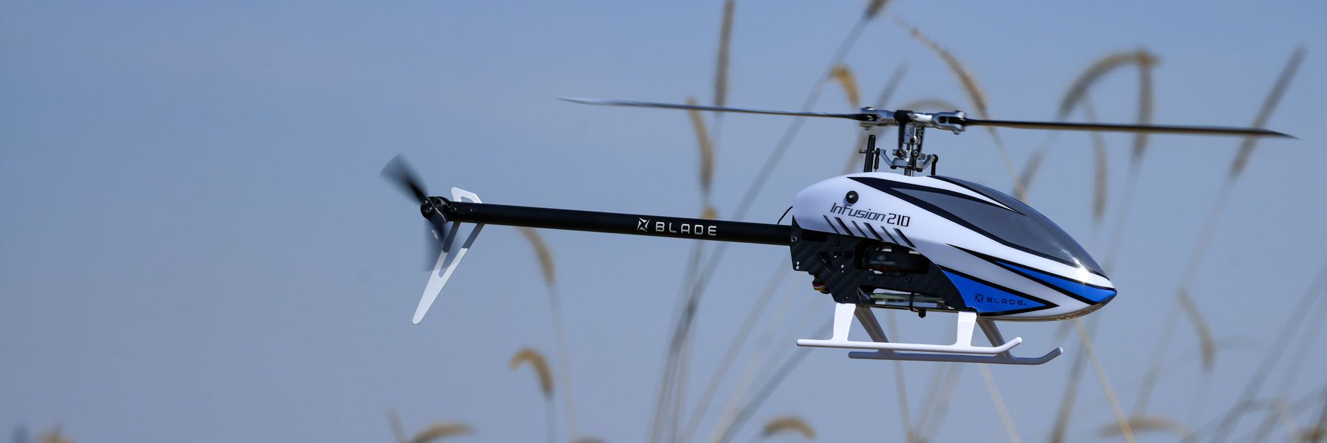 Action shot of the Blade InFusion 210 Bind-N-Fly Basic RC helicopter with AS3X and SAFE hovering in the air above a field