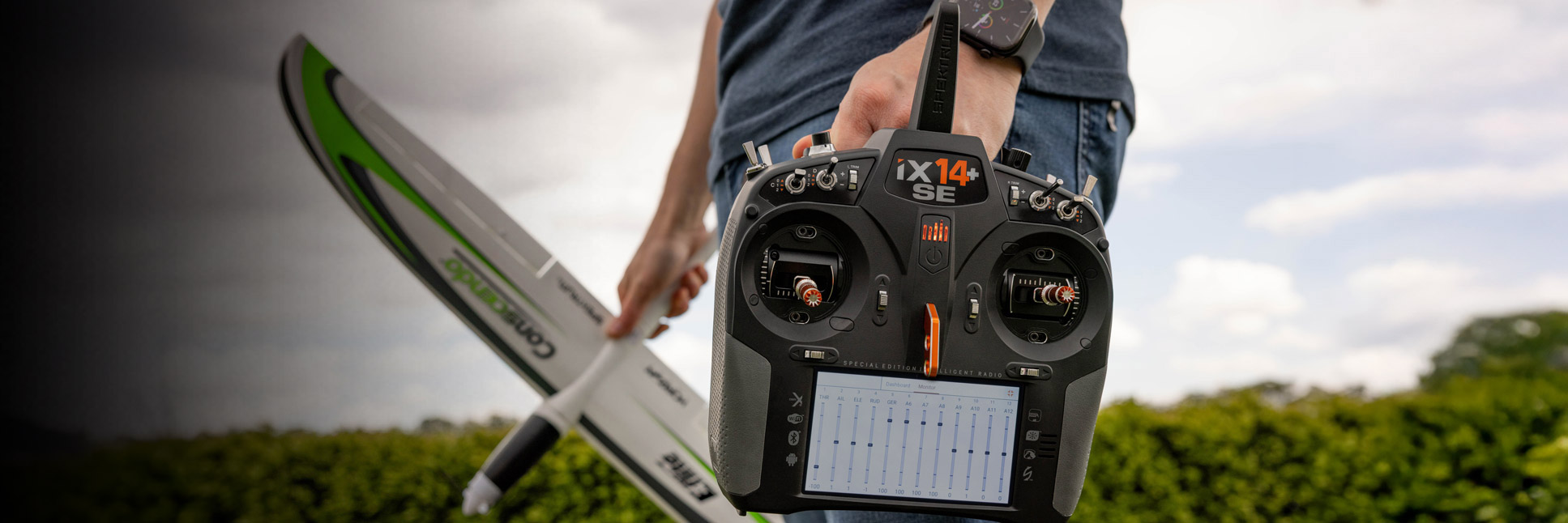Action shot of the Spektrum iX14+ SE 20-Channel DSMX Transmitter on a bench with a RC airplane in the background Action shot of the Spektrum iX14+ SE 20-Channel DSMX Transmitter on a bench with a RC airplane in the background